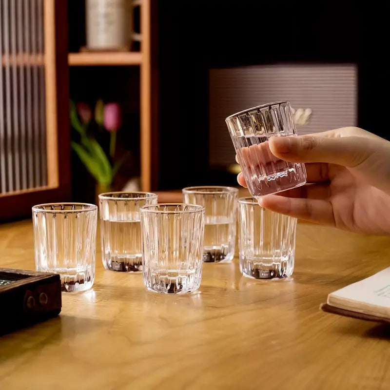 Hand holding a clear glass on a wooden table with other glasses.